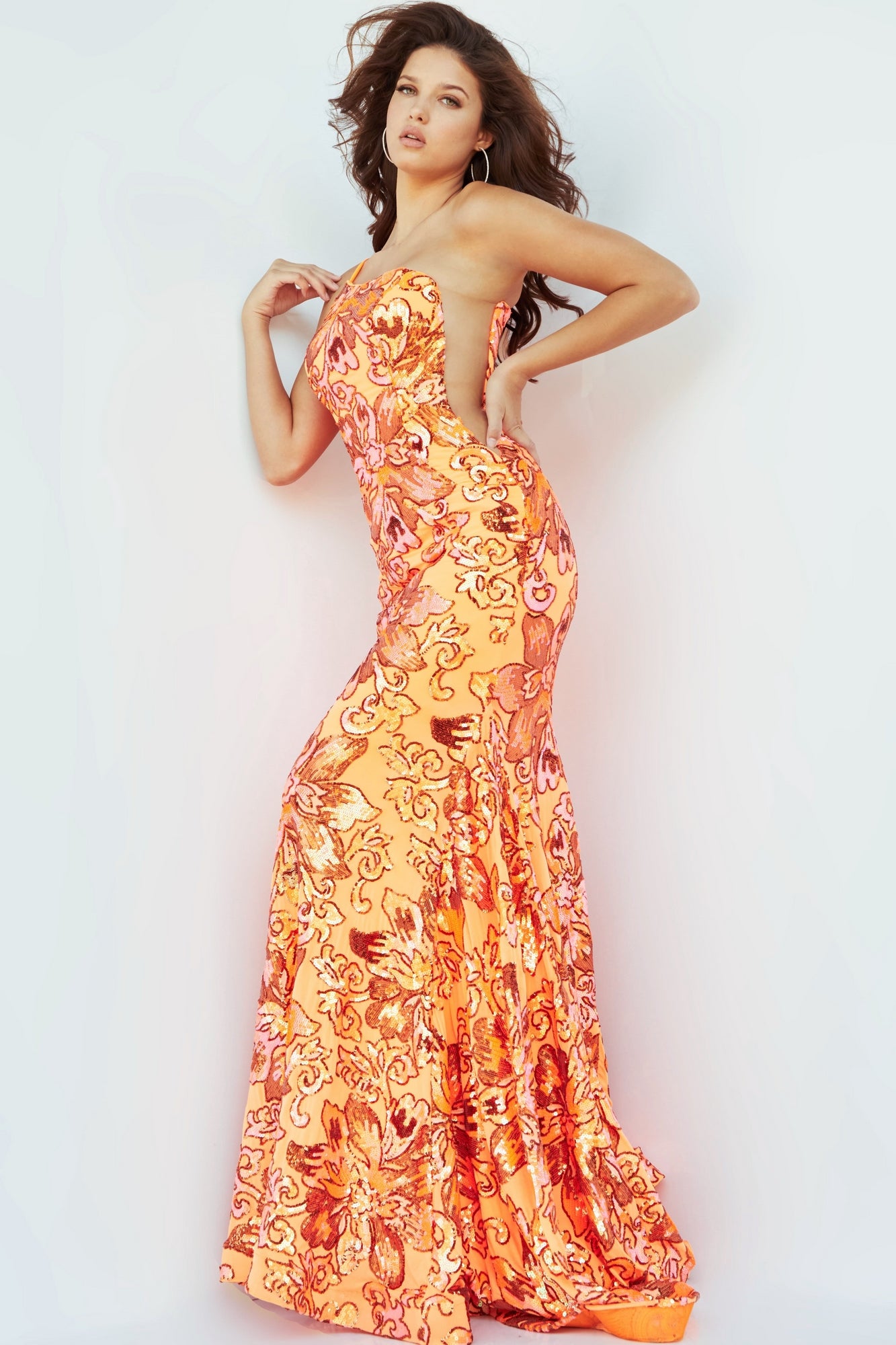 A woman poses in a one-shoulder Jovani prom dress adorned with floral sequins, standing against a plain white background.